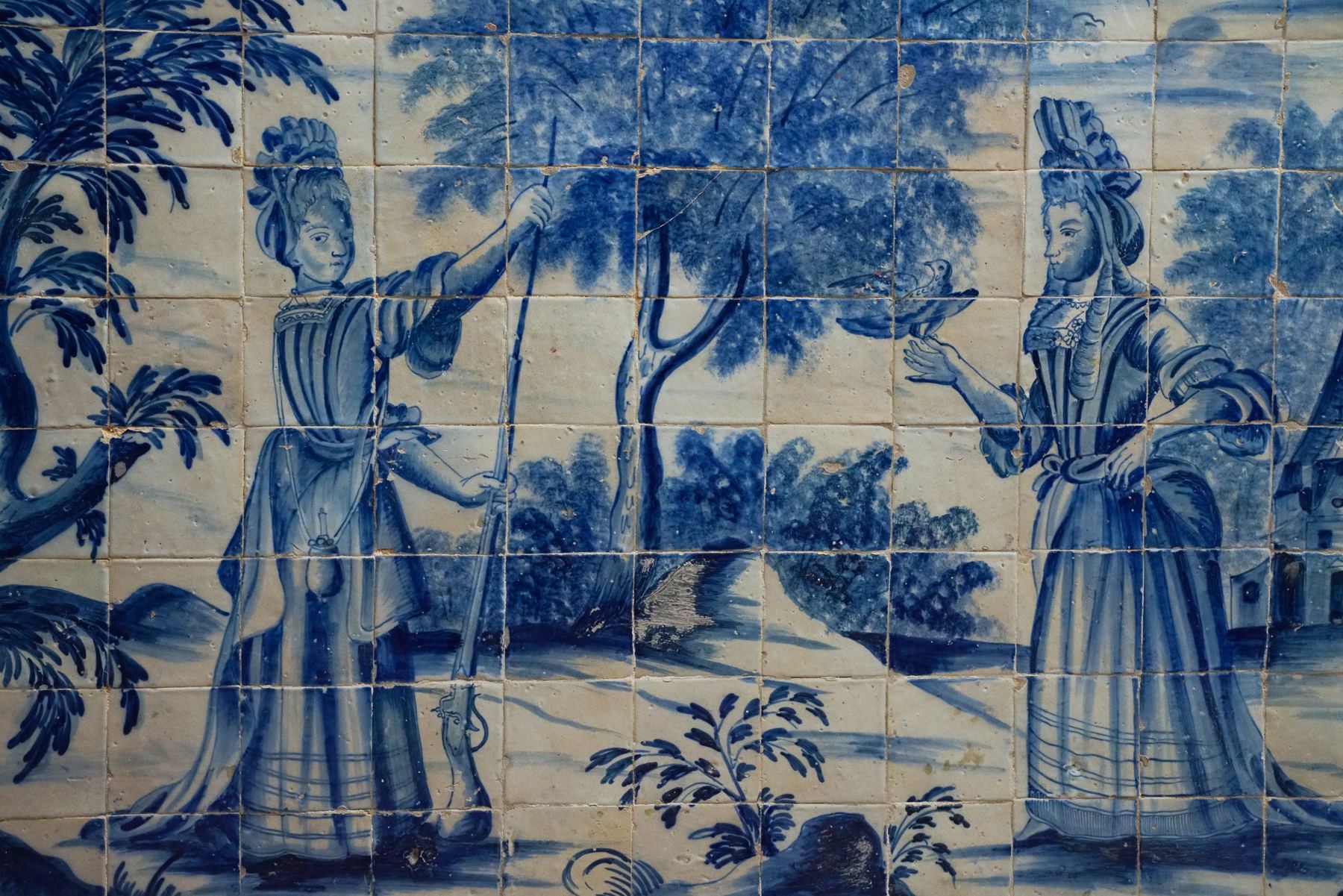 Azulejos tradicionais azuis e brancos retratam duas figuras femininas numa cena campestre no Palácio do Grilo, Lisboa.