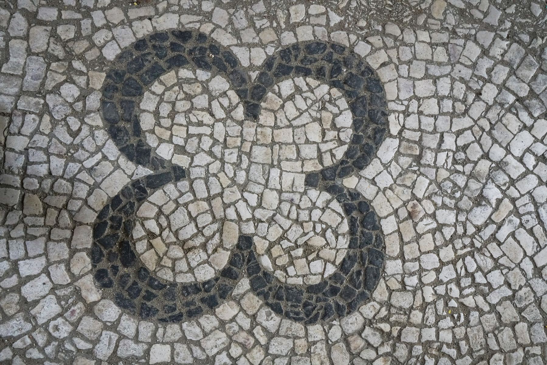 Pormenor de calçada portuguesa tradicional em preto e branco com um padrão orgânico no Palácio do Grilo, Lisboa.