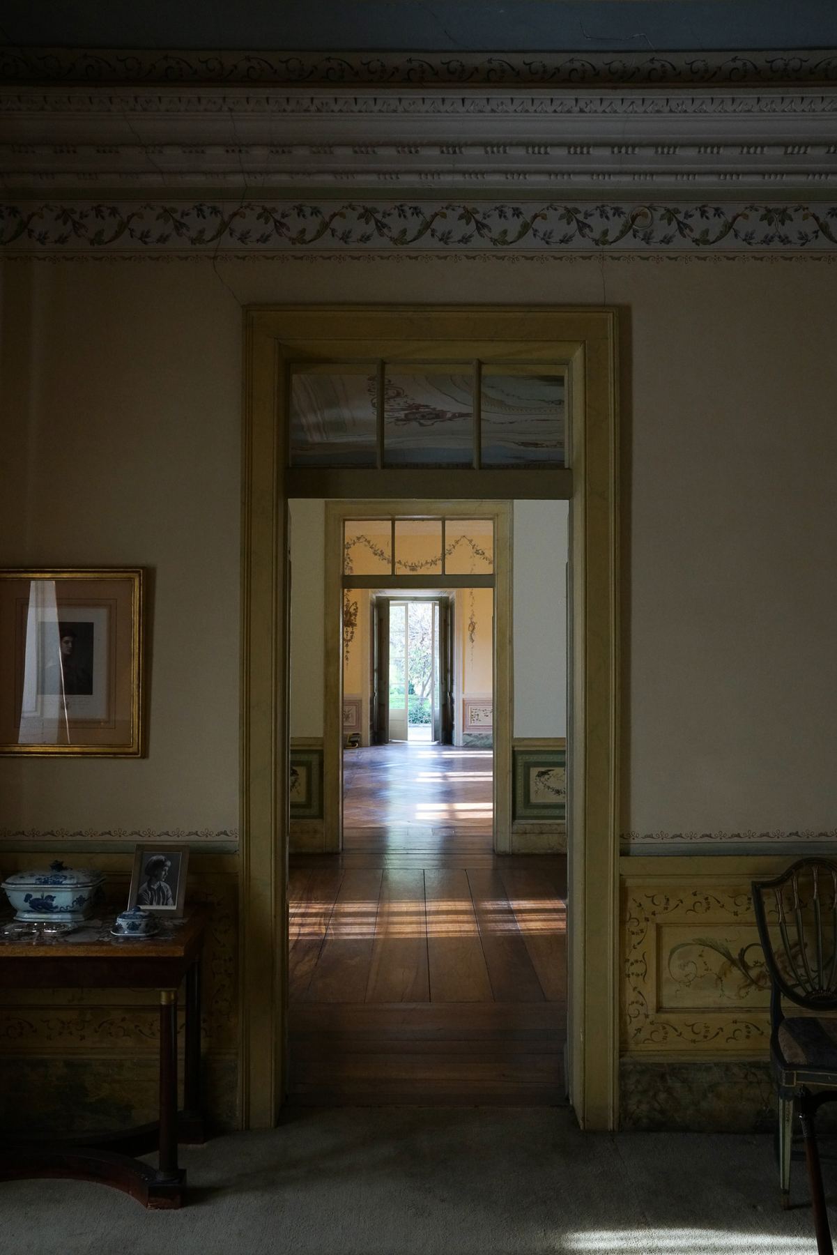 Uma vista através de múltiplos arcos e salas do Palácio do Grilo em Lisboa, com luz natural realçando o piso de madeira.