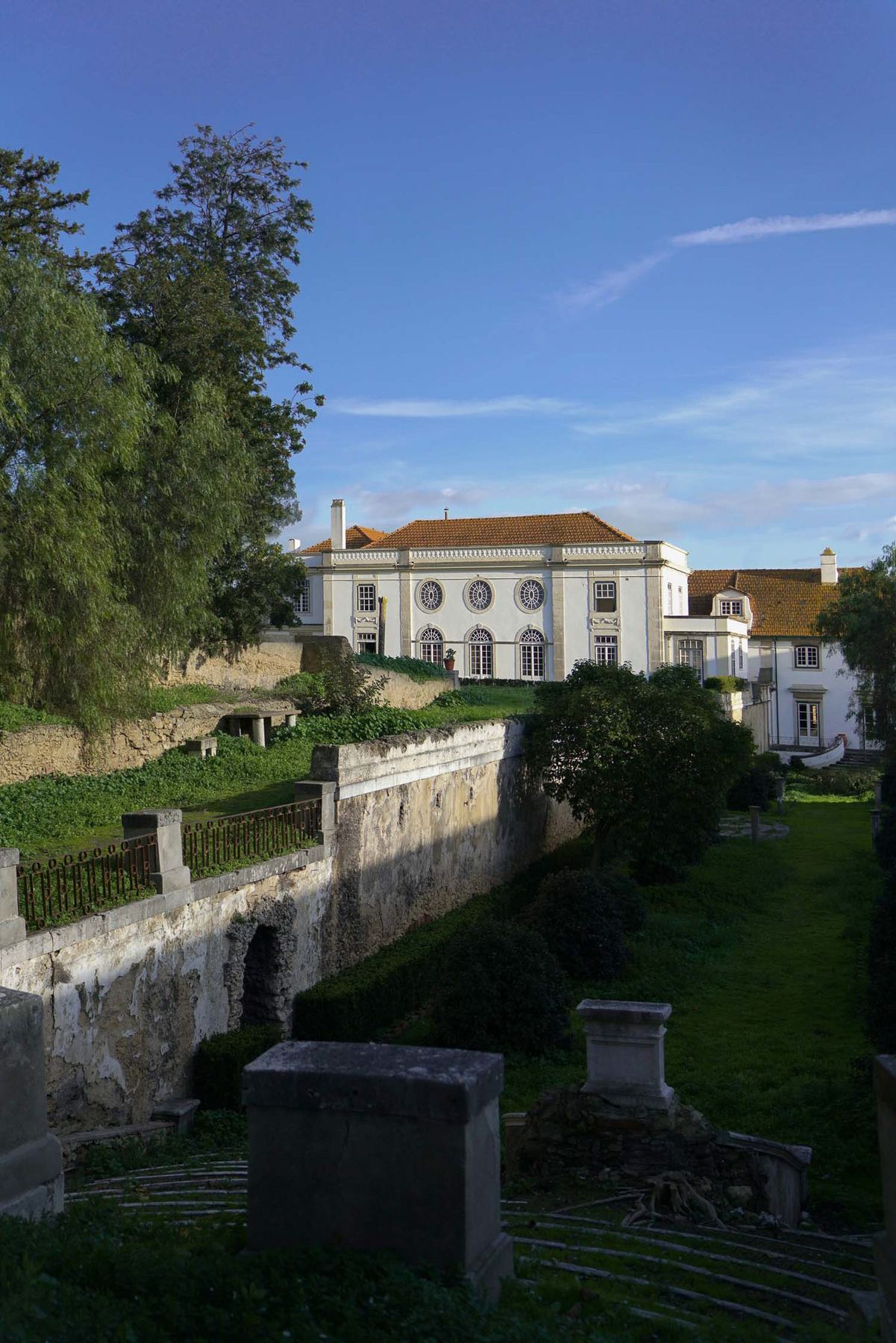 Vista exterior do Palácio do Grilo em Lisboa, mostrando a fachada clássica branca e os exuberantes jardins verdes.