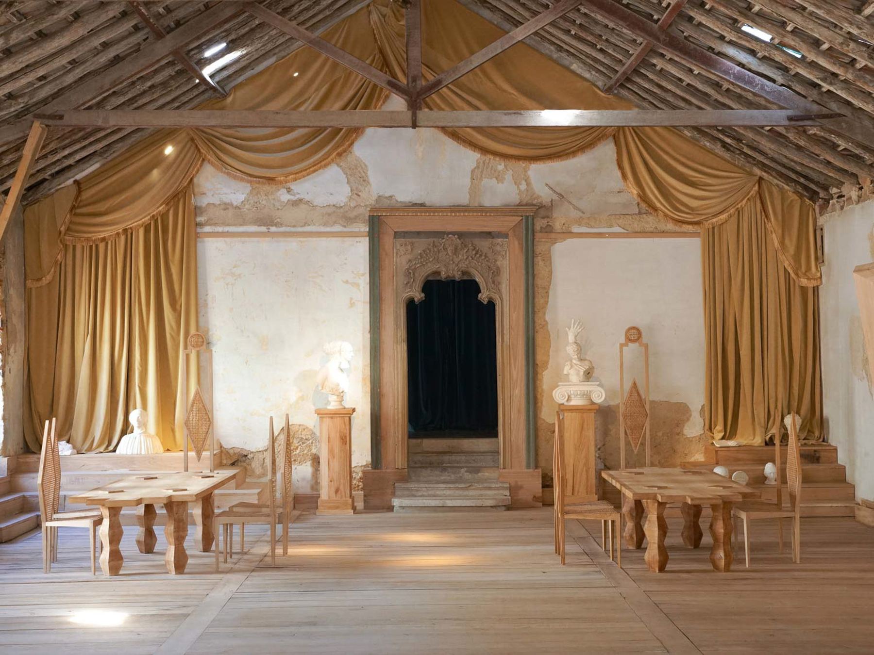 Um interior rústico e teatral do Palácio do Grilo, com cortinas douradas, móveis de madeira e telhado exposto em Lisboa.