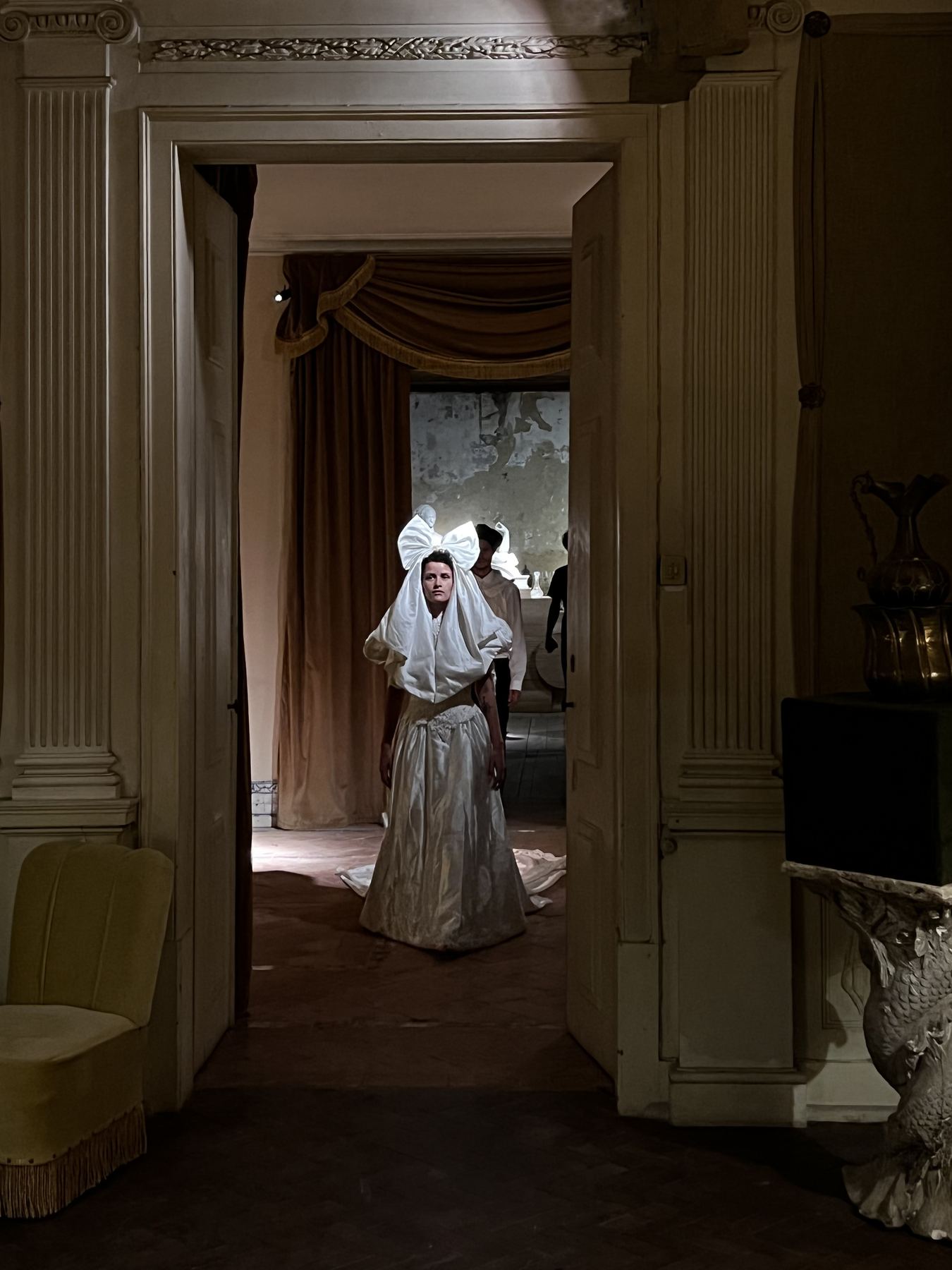 Uma pessoa vestida de branco com um laço grande na cabeça entra numa sala do Palácio do Grilo, em Lisboa.