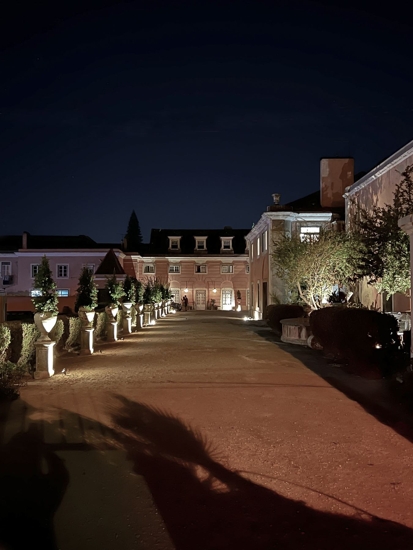 O Palácio do Grilo iluminado à noite, com um caminho alinhado por vasos e luzes, em Lisboa.