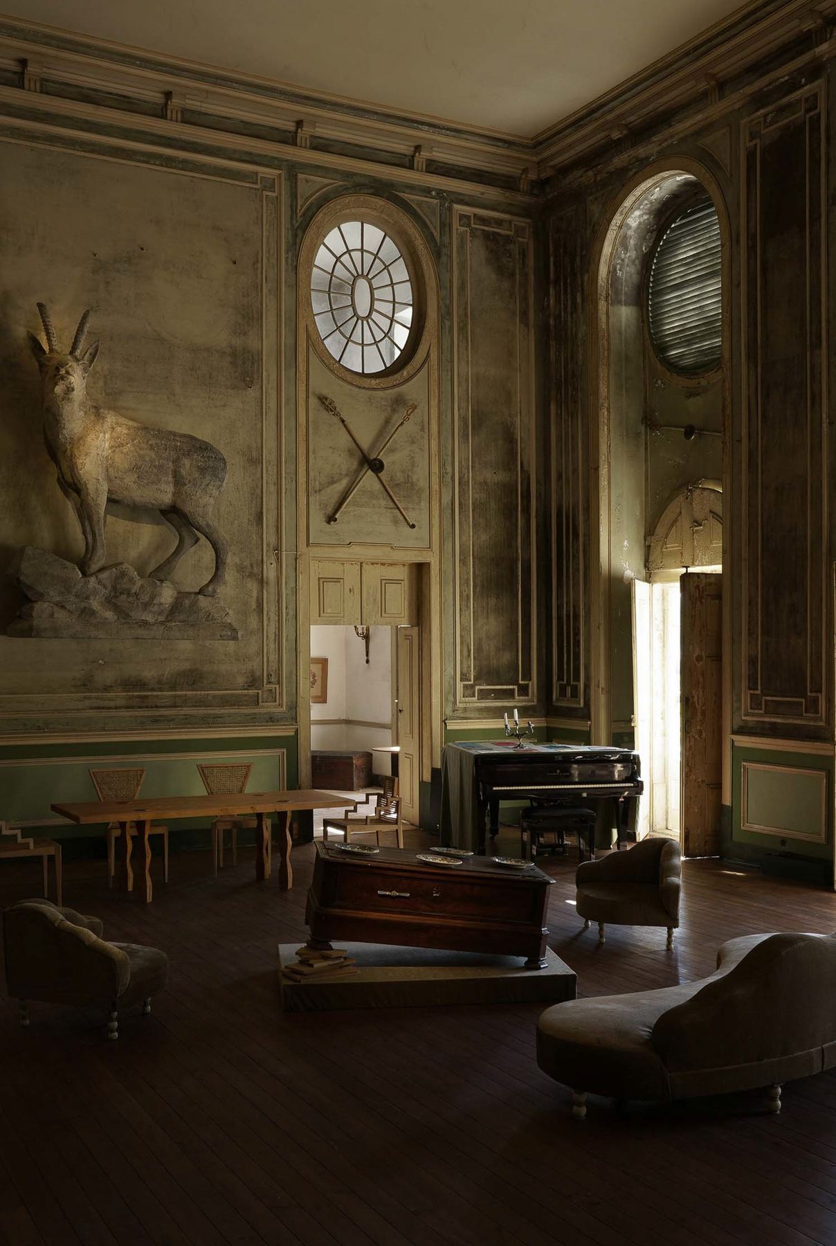 Um majestoso salão do Palácio do Grilo em Lisboa, com painéis ornamentados, um relevo de cervo, piano e mobiliário vintage.