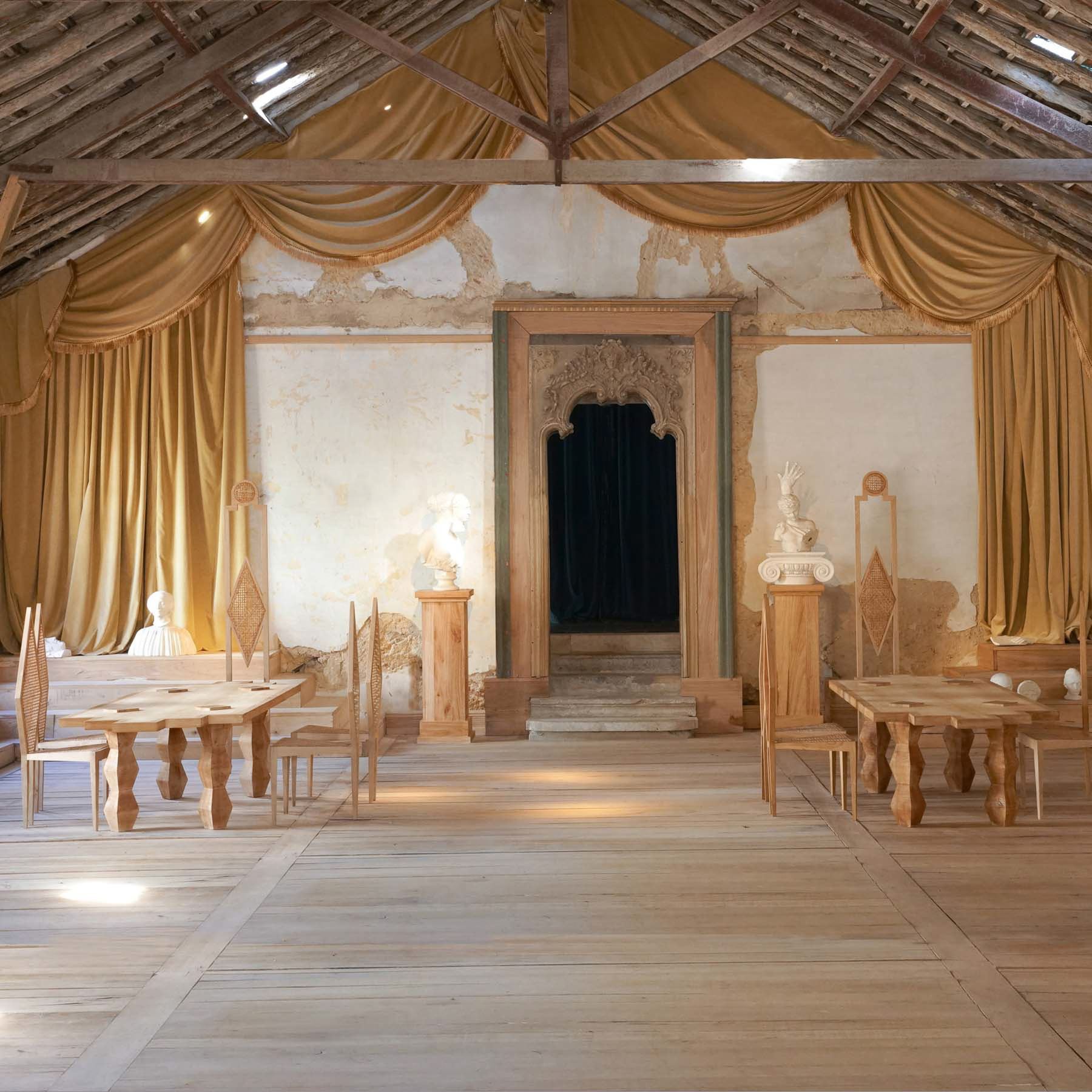 Um espaçoso salão rústico no Palácio do Grilo em Lisboa, com móveis de madeira clara e tapeçarias douradas no teto.