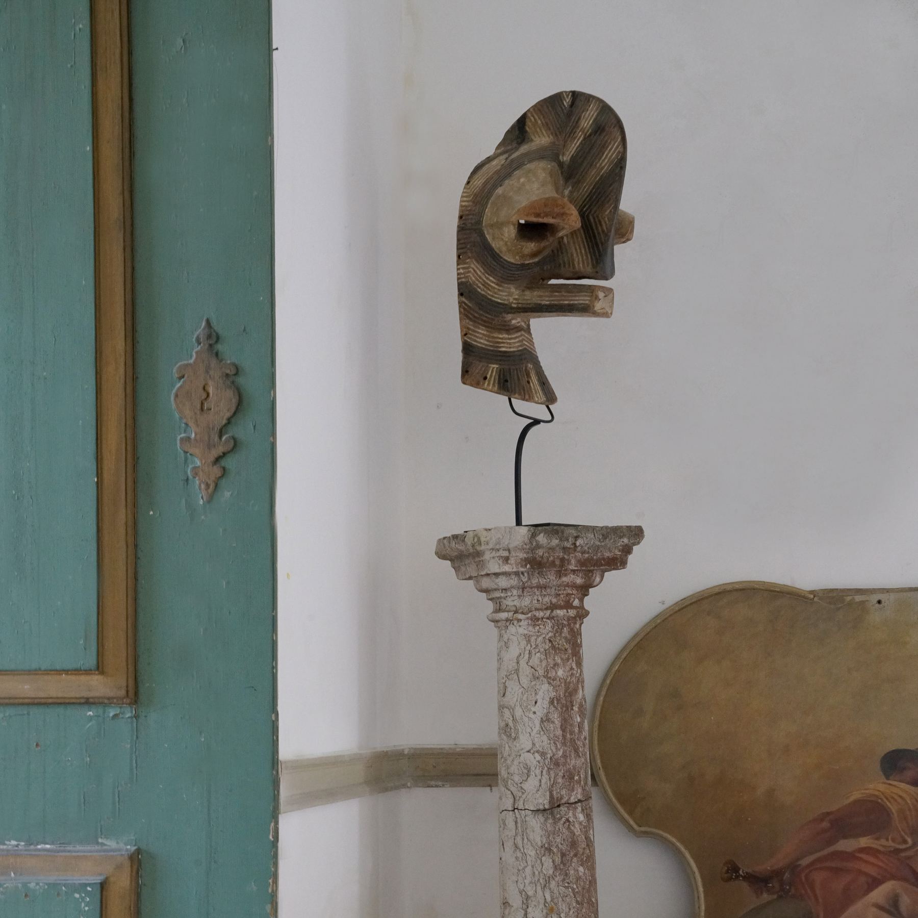 Uma máscara esculpida sobre uma coluna de pedra decora o Palácio do Grilo em Lisboa, perto de uma porta turquesa.