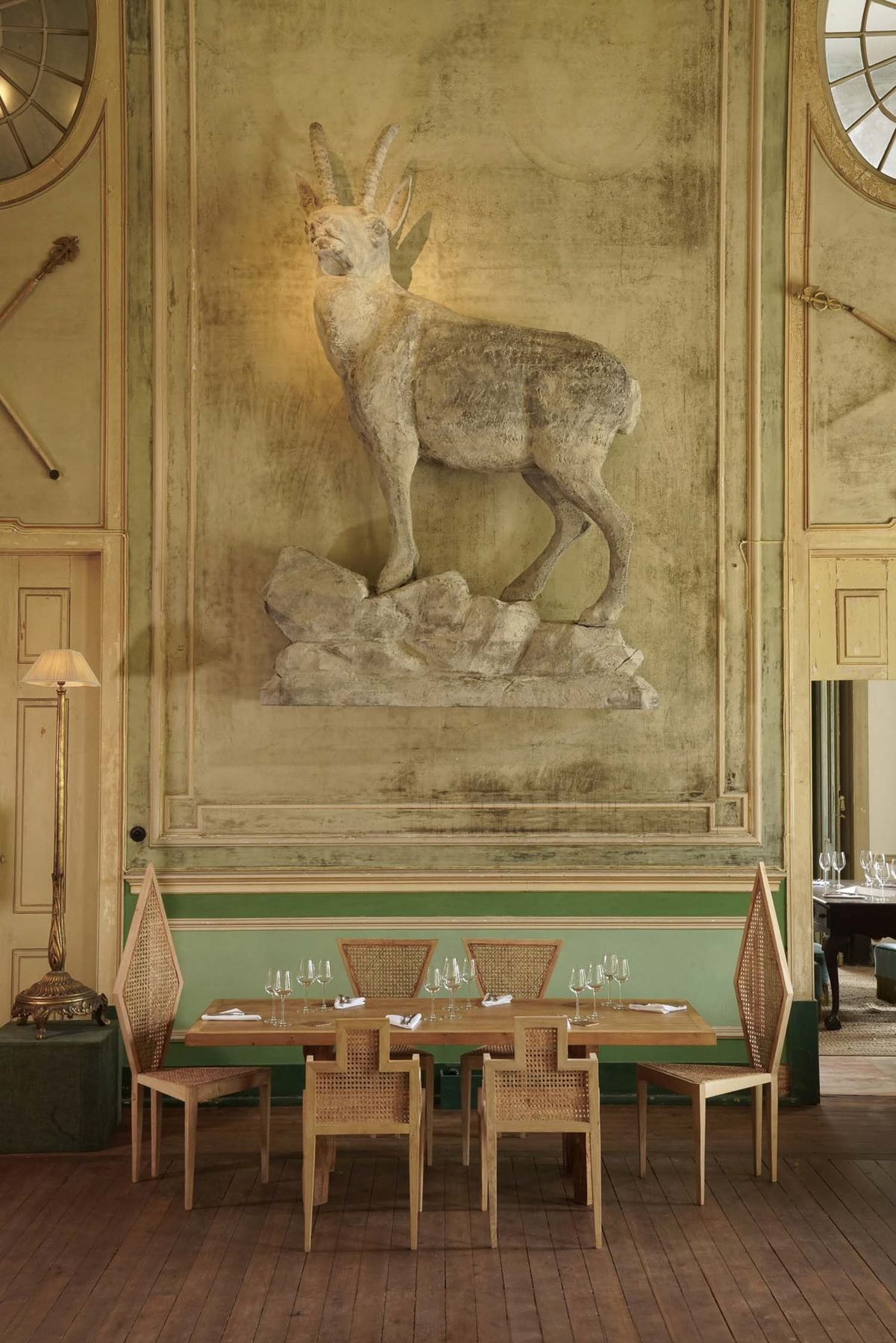 Um relevo de cabra montesa domina a sala de jantar do Palácio do Grilo, em Lisboa, com mesas de vime e madeira.