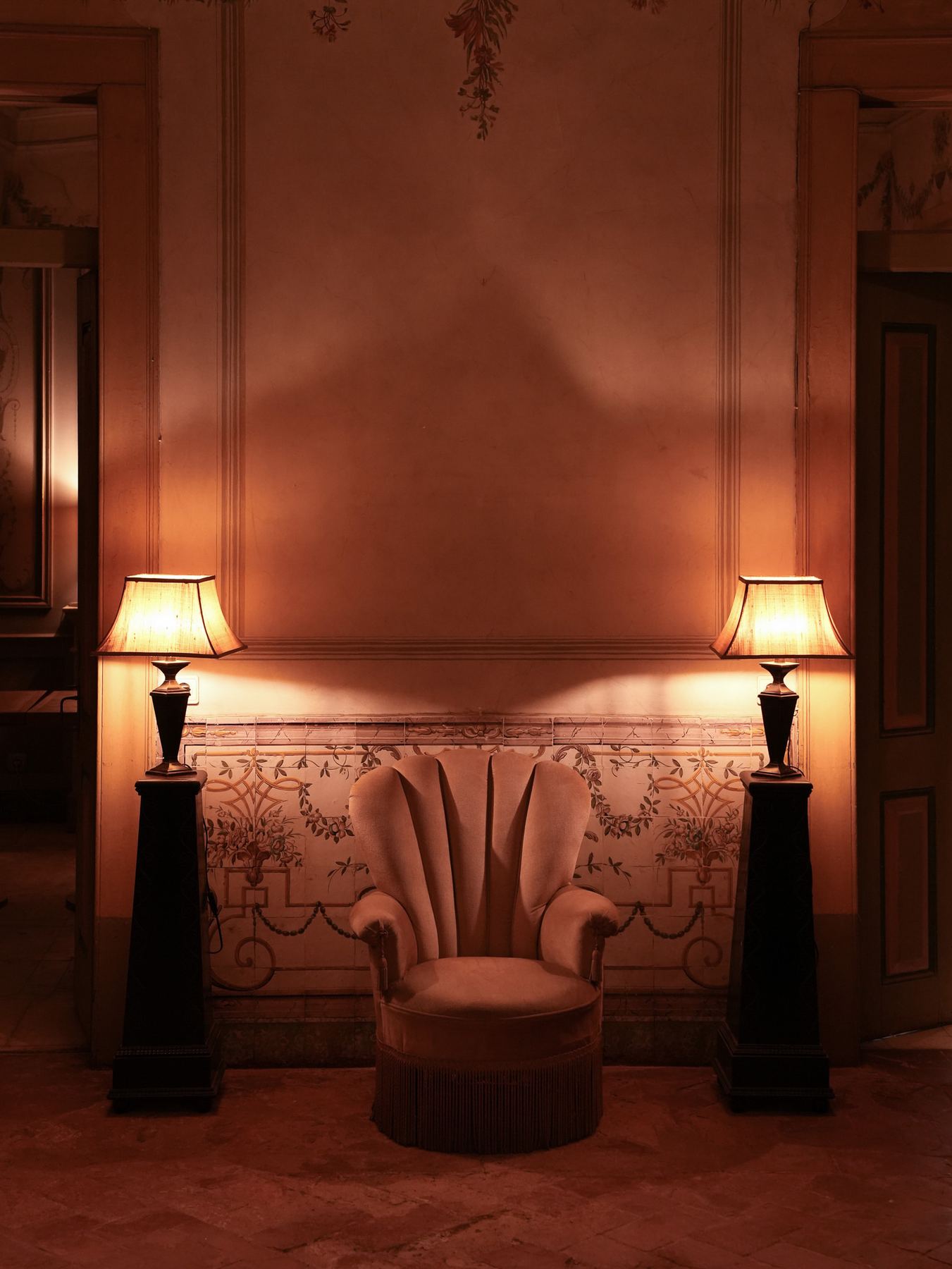 Poltrona de veludo rosa iluminada por duas lâmpadas em ambiente acolhedor do Palácio do Grilo, Lisboa.