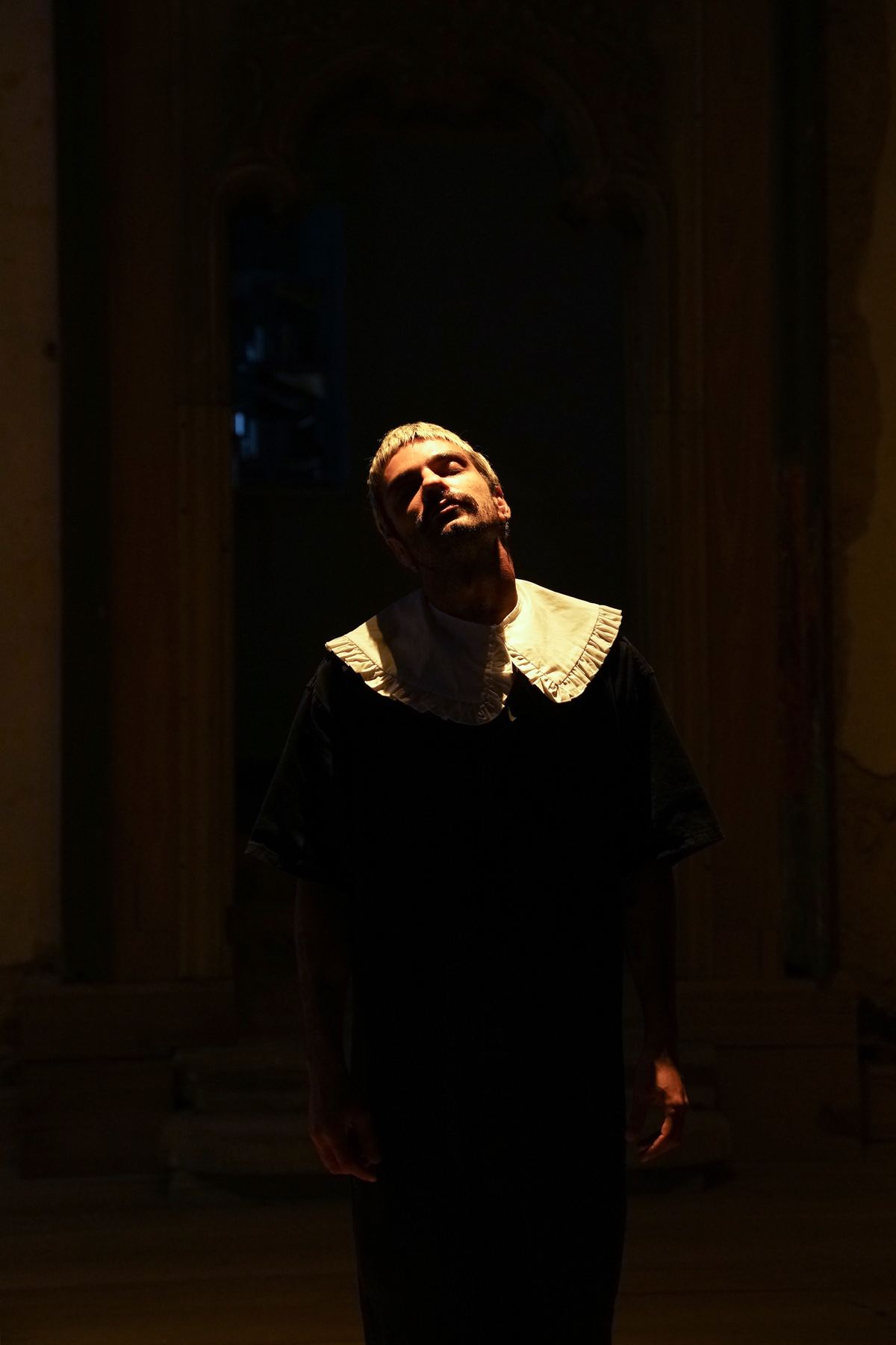 Um homem de gola branca, sob uma luz dramática, posa num ambiente escuro do Palácio do Grilo em Lisboa.