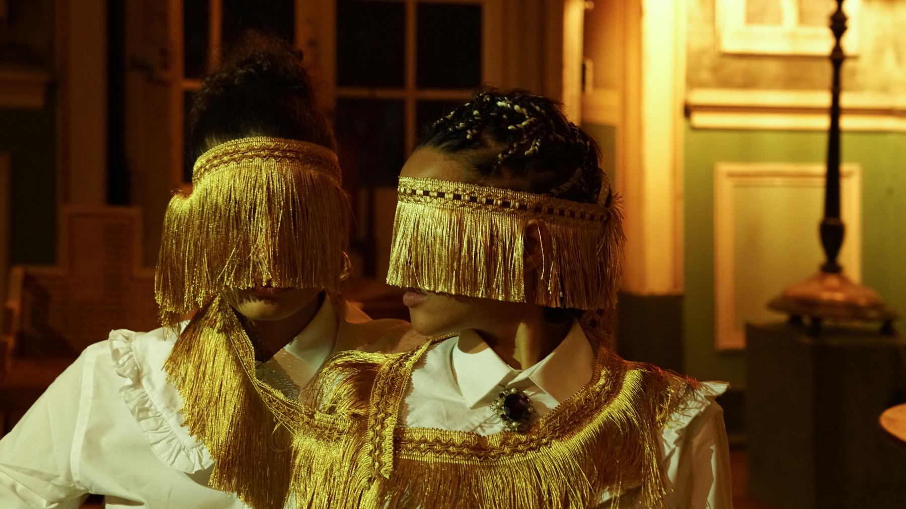 Duas figuras com elaborados trajes dourados com franjas, destacando a atmosfera única do Palácio do Grilo em Lisboa.