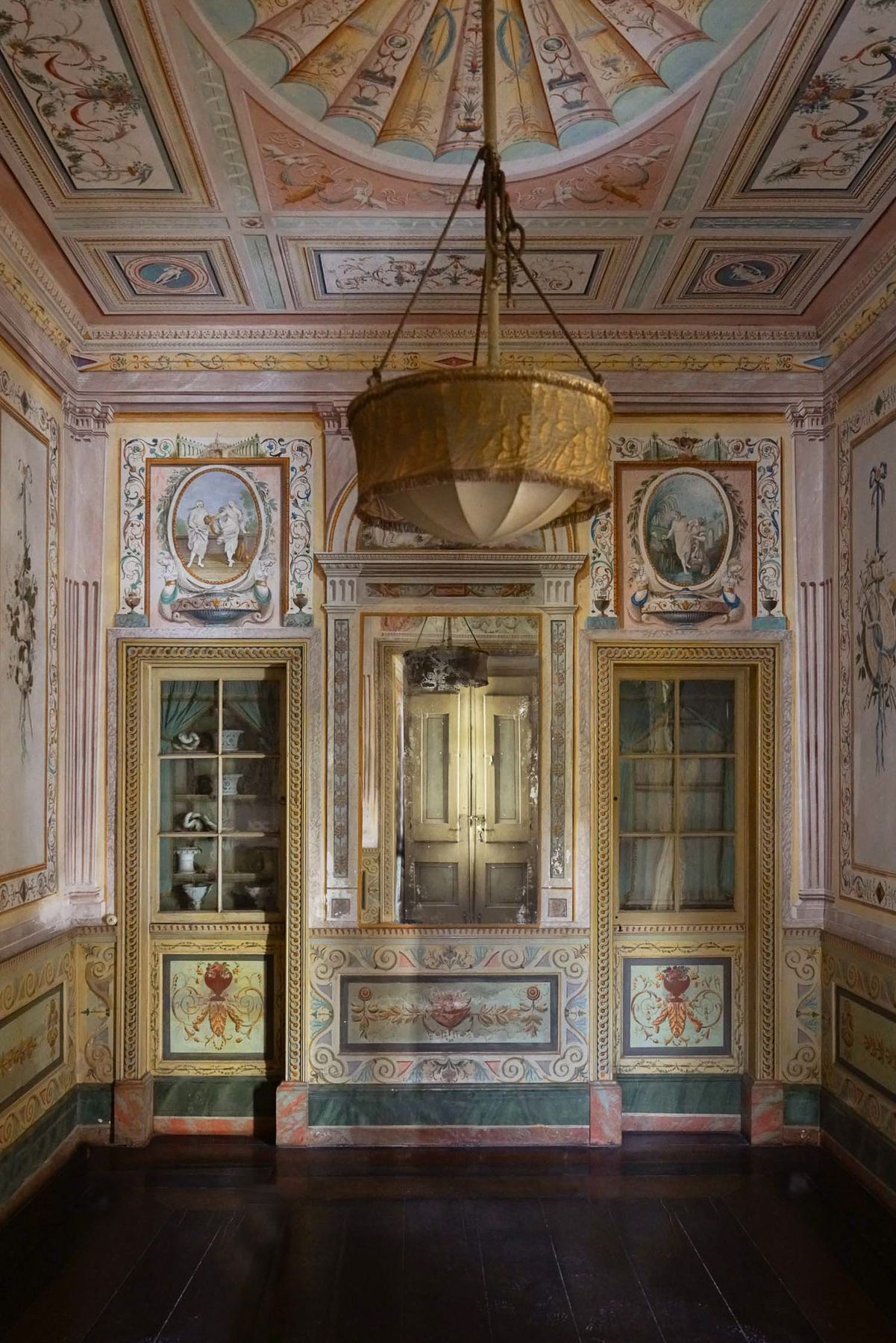 Um salão ricamente pintado do Palácio do Grilo em Lisboa, com teto barroco e paredes ornamentadas, iluminado por um lustre.