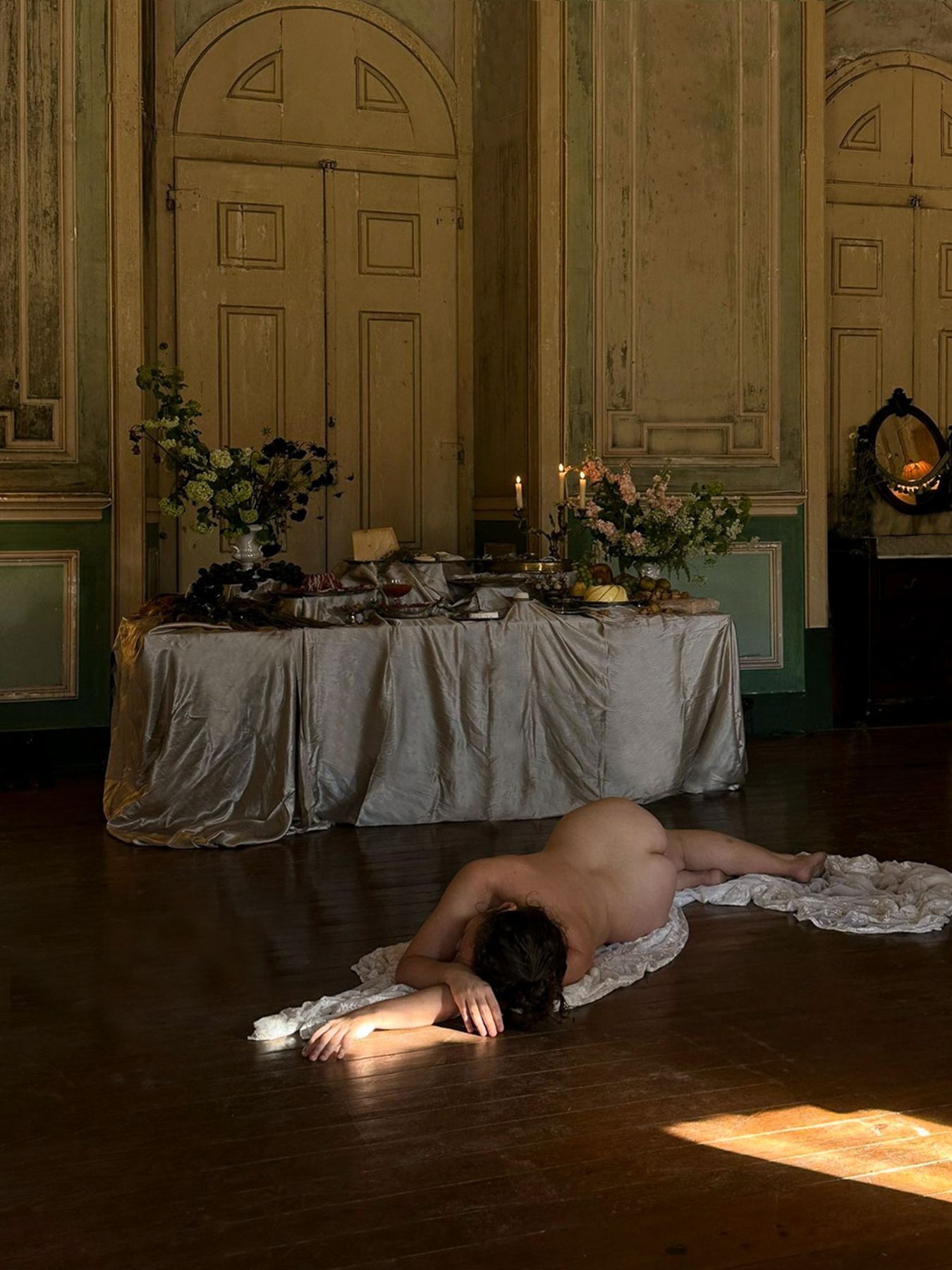 Corpo nu repousa no chão de madeira escura do Palácio do Grilo, em Lisboa, à frente de uma mesa.