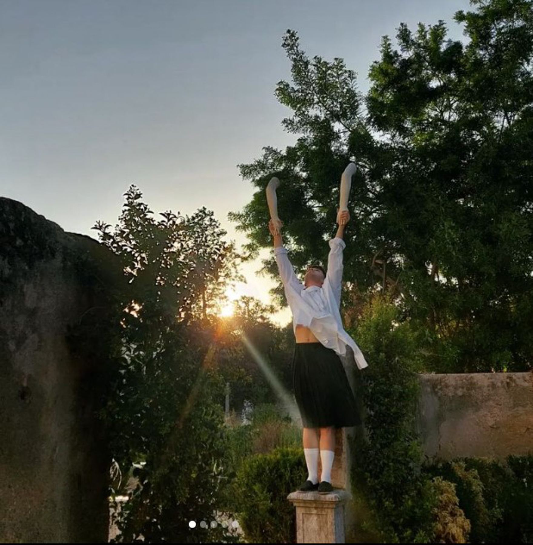 Pessoa com camisa e saia levantando os braços, exibindo performance no exterior do Palácio do Grilo em Lisboa ao pôr do sol.