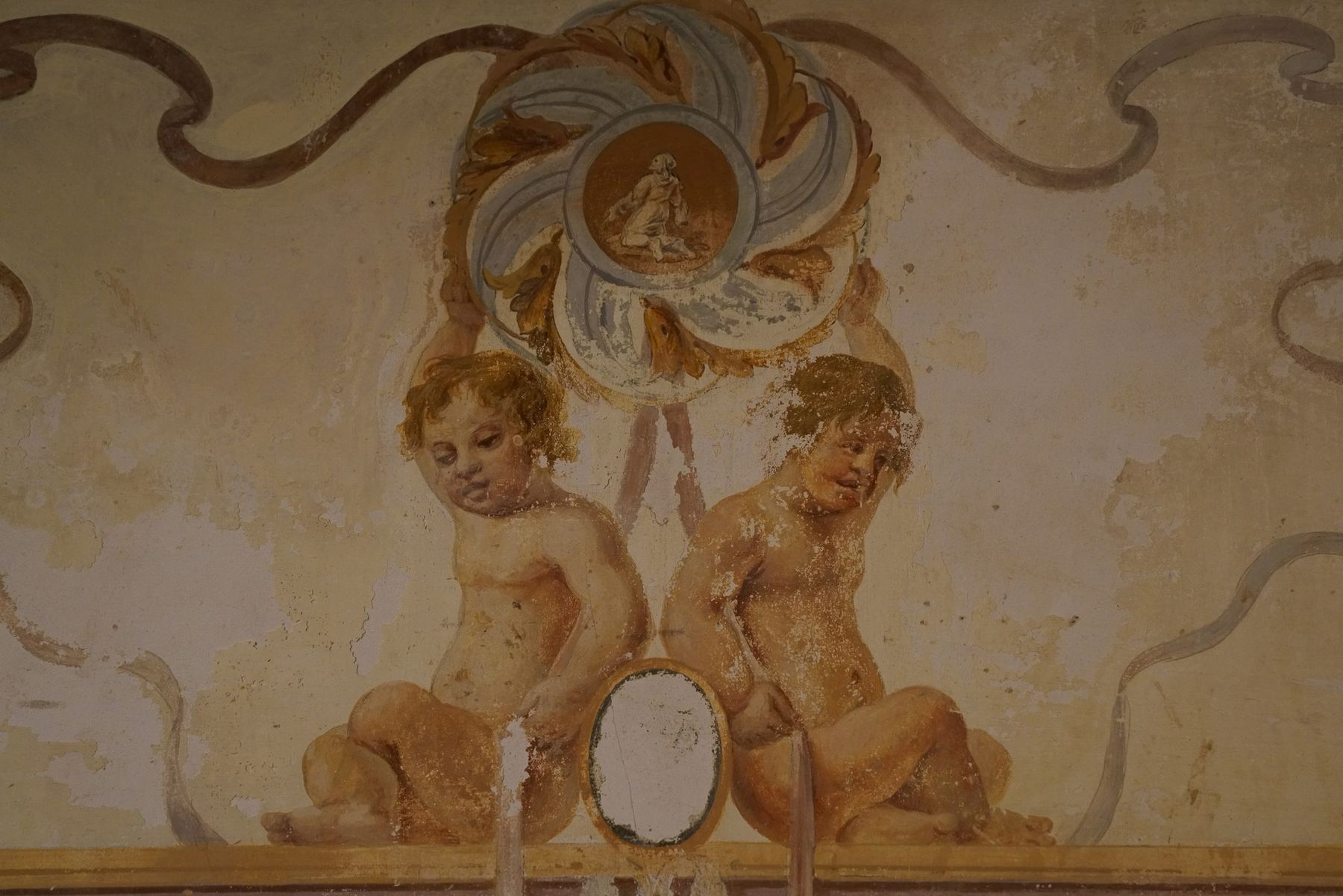 Um detalhe de afresco barroco no Palácio do Grilo, mostrando dois querubins envelhecidos com um medalhão central em Lisboa.